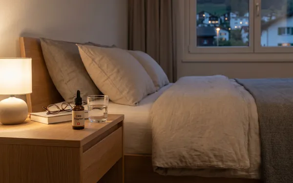 Nachttisch in einem Schweizer Schlafzimmer mit neutral beschrifteter CBD-Tropfen-Flasche und Glas Wasser als Teil einer abendlichen Schlafroutine